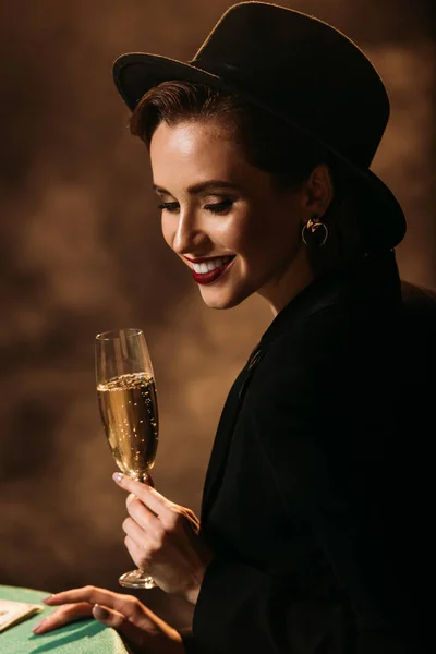Улыбающаяся Привлекательная Девушка Куртке Шляпе Бокалом Шампанского Покерным Столом Казино — Бесплатное стоковое фото