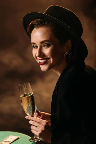 Sorridente Ragazza Attraente Giacca Cappello Possesso Bicchiere Champagne Tavolo Poker — Foto stock gratuita