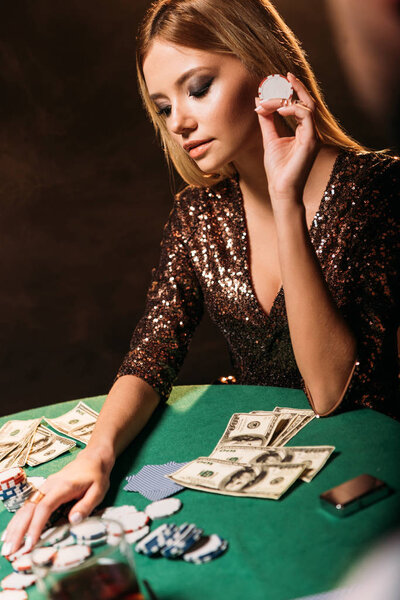 attractive girl holding poker chip and looking at table at casino