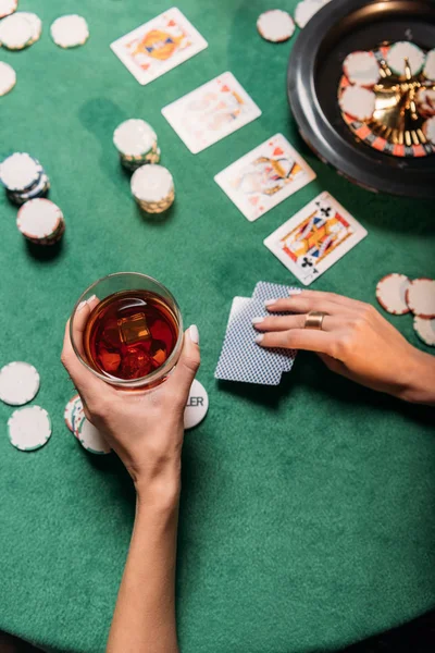 ポーカーとカジノのテーブルで ウィスキーのグラスを押しの女の子のトリミングされたイメージ  — 無料ストックフォト