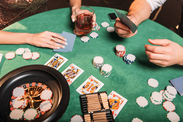 обрезанный образ девушки и крупье, играющих в покер за столом в казино
