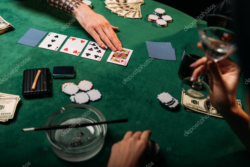 Cropped image of woman and tattooed man playing poker table in casino, girl holding glass of cocktail