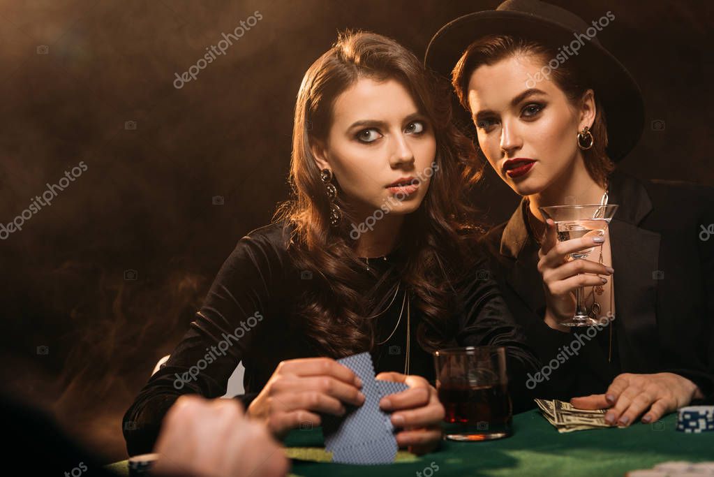 Beautiful women playing poker at table in casino and looking away