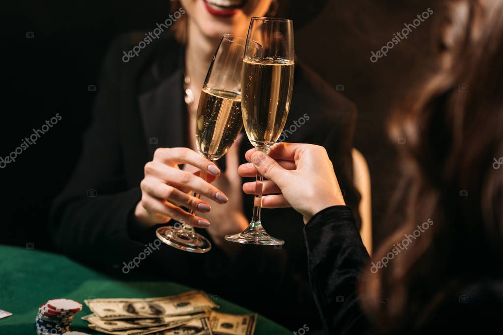 Cropped image of happy girls clinking with glasses of champagne at poker table in casino