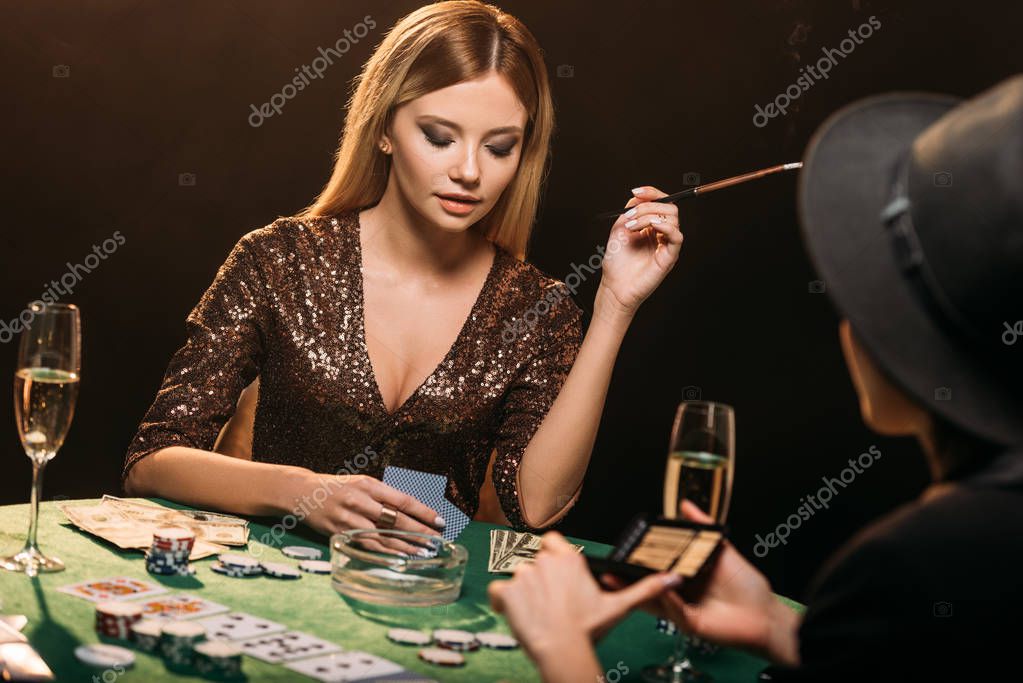 Attractive girls smoking cigarettes and playing poker at table in casino