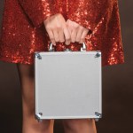 Cropped image of girl in red shiny dress holding money box isolated on black