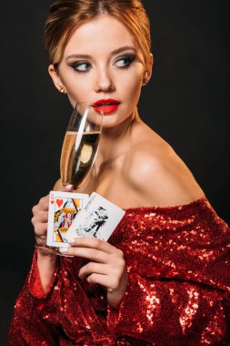 attractive girl in red shiny dress holding joker and queen of hearts cards, drinking champagne isolated on black clipart