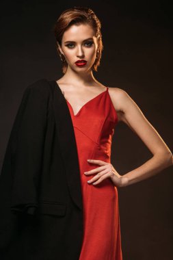 beautiful woman in red dress and black jacket on one shoulder looking at camera isolated on black clipart