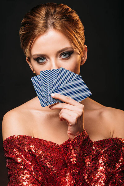 attractive girl in red shiny dress looking out from playing cards isolated on black