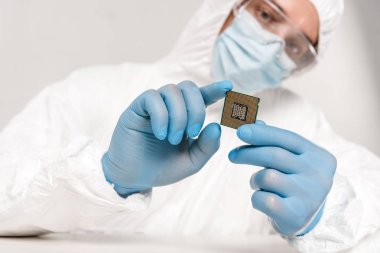 selective focus of microprocessor in hands of scientist in googles on grey background clipart