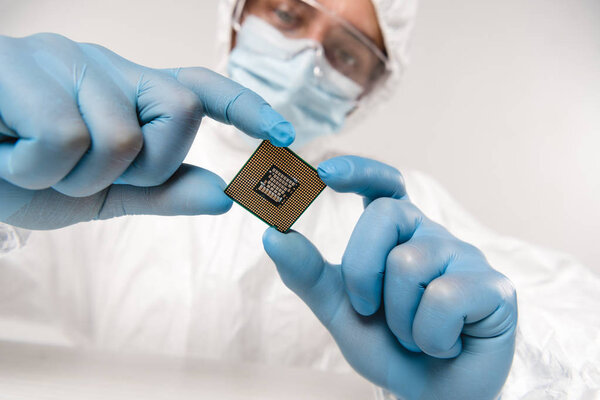 selective focus of microchip in hands of scientist wearing latex gloves, googles and mask on grey background