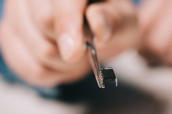 selective focus of tweezers with microchip in hand of man