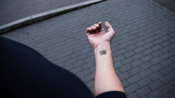 обрезанный вид человека со штрих-кодом на руке с кирпичами на заднем плане
 