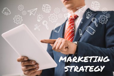 cropped view of businessman using digital tablet with marketing strategy icons