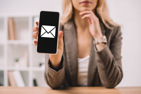 cropped view of businesswoman presenting smartphone with email icon 