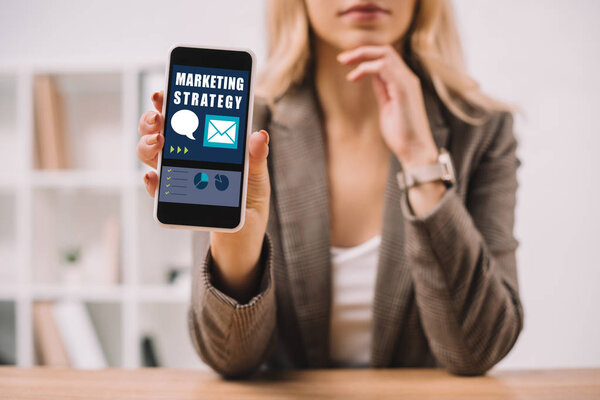 cropped view of businesswoman presenting smartphone with marketing strategy