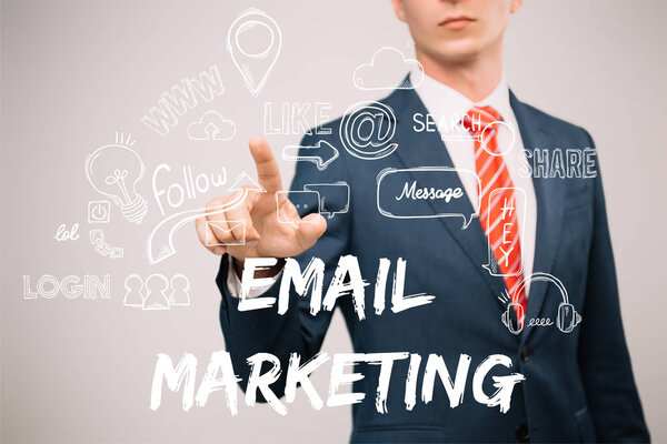 cropped view of businessman in suit pointing at email marketing icons isolated on grey