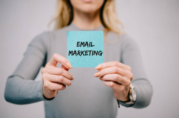 cropped view of woman holding blue paper note with email marketing isolated on grey