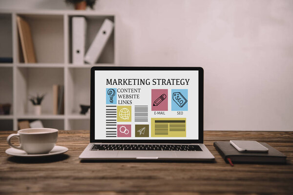 ноутбук с маркетинговой стратегией, смартфон и чашка кофе на деревянном столе

