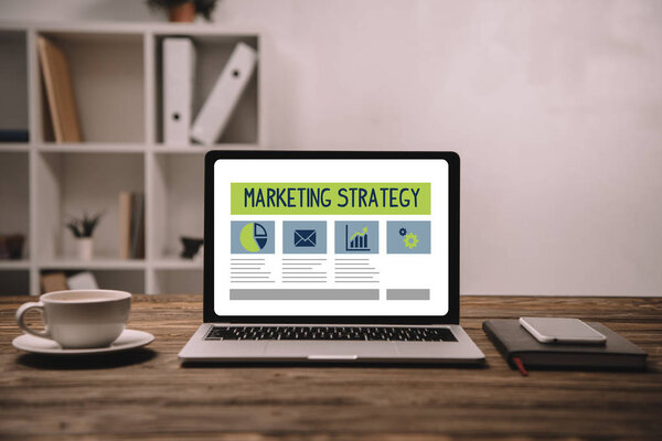 ноутбук с маркетинговой стратегией, смартфон и чашка кофе на деревянном столе
