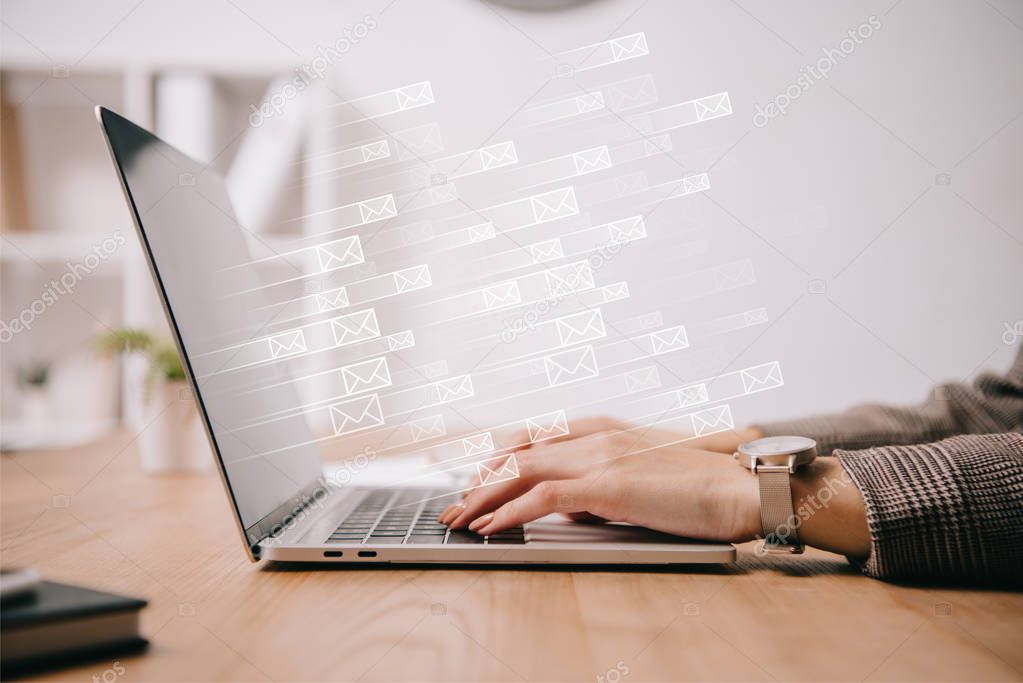 cropped view of businesswoman working and typing on laptop with sending e-mails icons