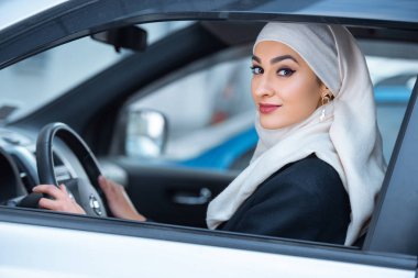 arabada oturan ve kameraya gülümseyen genç Müslüman kadın 