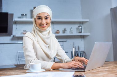 beautiful young muslim woman using laptop and smiling at camera clipart