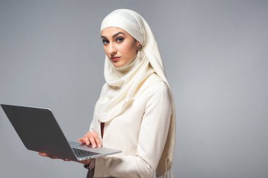 dizüstü bilgisayar kullanarak ve gri izole kamera bakarak genç Müslüman kadın