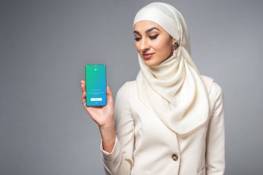 Smartphone gri izole twitter uygulaması ile tutan güzel gülümseyen genç Müslüman kadın