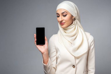 Smartphone ile boş ekran gri izole tutan güzel gülümseyen genç Müslüman kadın