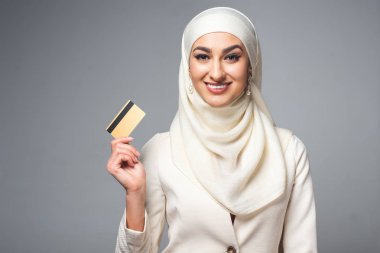 kredi kartı tutan ve gri izole kamera gülümseyen güzel Müslüman kadın 