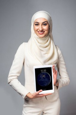 Dijital tablet tutarak ve gri izole kamera gülümseyen genç Müslüman kadın  