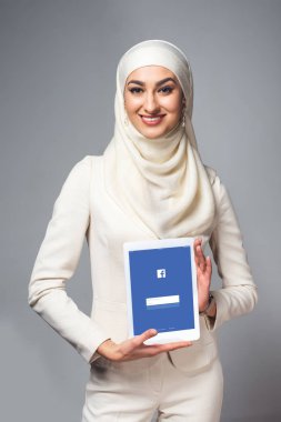 Dijital tablet facebook app ile tutarak ve gri izole kamera gülümseyen genç Müslüman kadın 