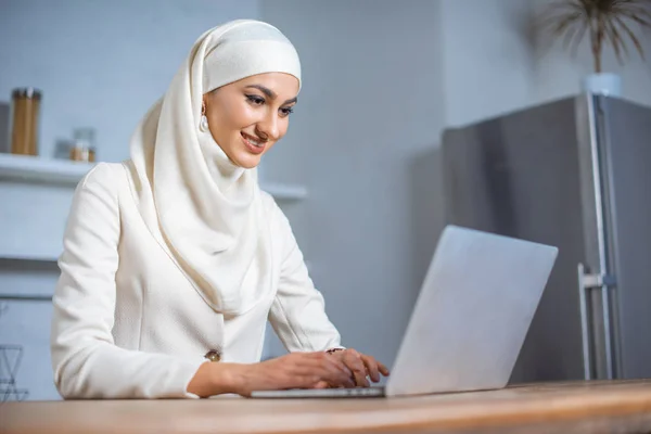 微笑的年轻穆斯林妇女使用笔记本电脑在家里 — 图库照片