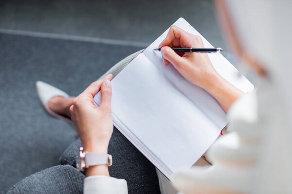 cropped shot of young woman writing in blank notepad at home