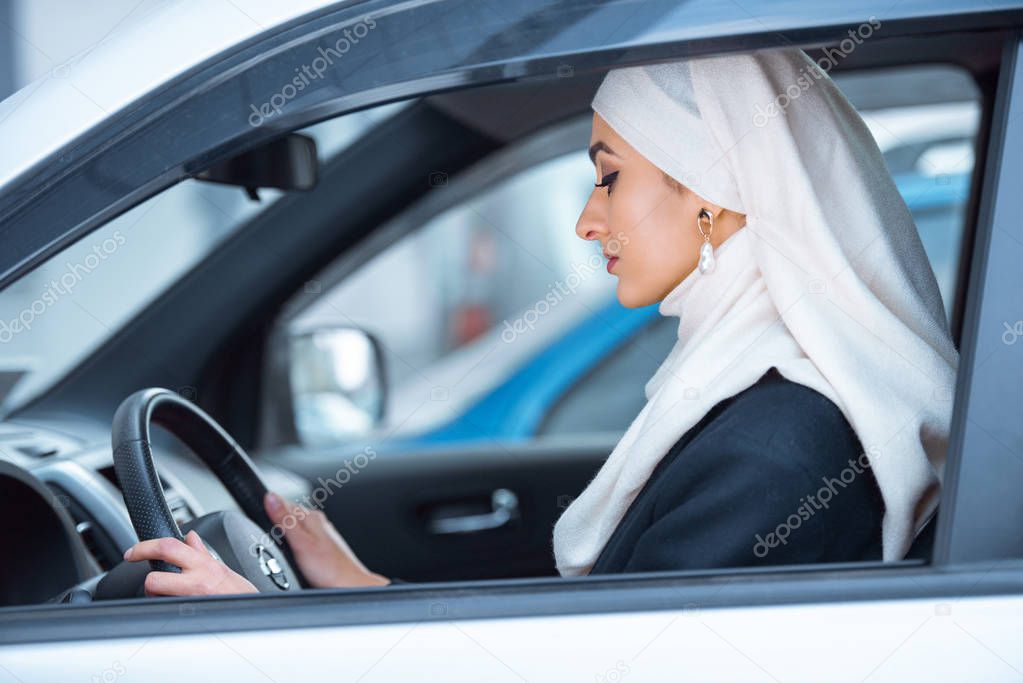 side view of beautiful young muslim woman driving car