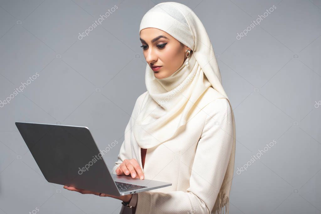 young muslim woman using laptop isolated on grey 