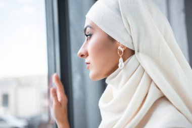 dalgın genç Müslüman kadın penceresine bakarak profil portresi   