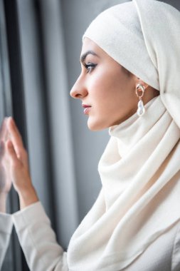 güzel genç Müslüman kadın penceresine bakarak yan görünüm  