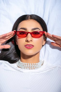 güzel esmer kız yatakta yatarken ve kameraya bakarak kırmızı güneş gözlüğü üstten görünüm 