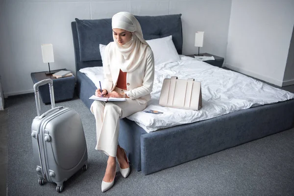 ベッドの上に座って ノートに書く若いイスラム教徒の女性のハイアングル — ストック写真