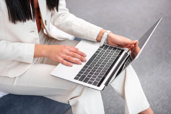 裁剪拍摄的年轻女子在时尚的白色西装使用笔记本电脑在家里 — 图库照片