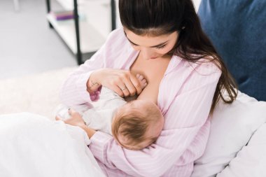 Genç anne emzirme portresi evde yatakta küçük bebek