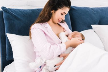 Genç anne emzirme portresi evde yatakta küçük bebek