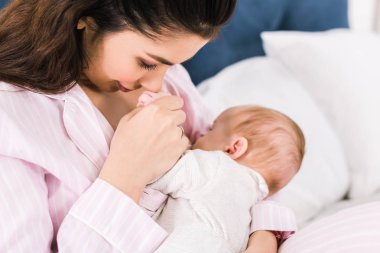Genç anne emzirme portresi evde yatakta küçük bebek