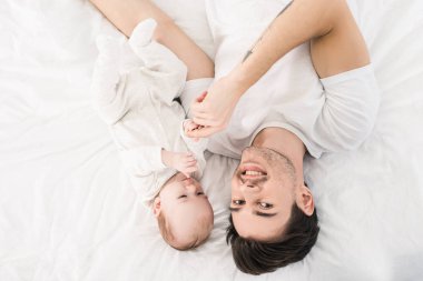 Baba ve küçük bebek yatakta birlikte evde yatarken gülümseyen havai görünümü