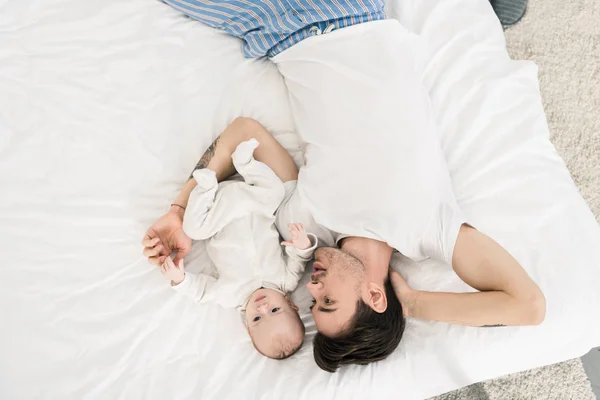 若い父親と家庭で一緒にベッドの上に横たわる小さな赤ちゃんのオーバー ヘッド ビュー — ストック写真