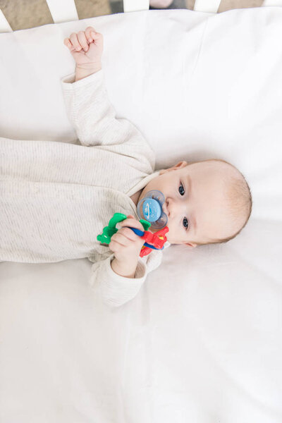 overhead view of little baby with pacifier holding toy while lying in crib