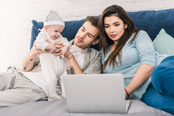 young woman using laptop while husband spending time with little son near by