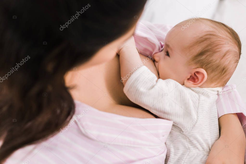 partial view of mother breastfeeding little baby at home